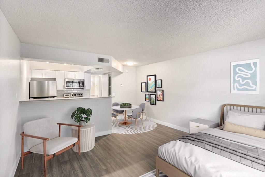 A bedroom with a bed, chair, and a small kitchenette.