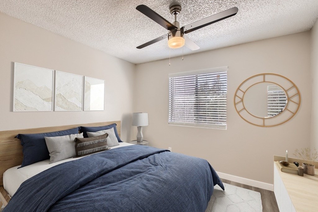 A bedroom with a bed, a ceiling fan, and a round mirror on the wall.
