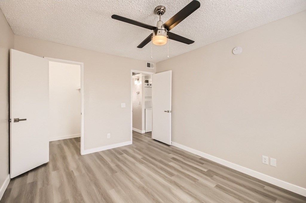 A room with a ceiling fan and light, wooden floors, and white walls.