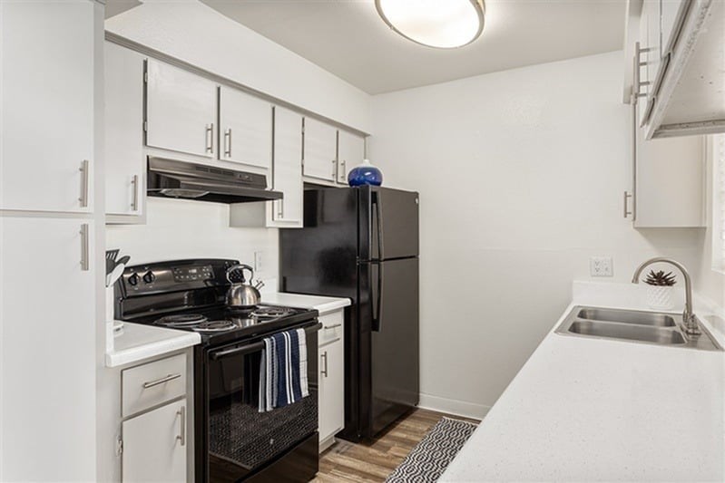 A black fridge sits in a kitchen with white cabinets.