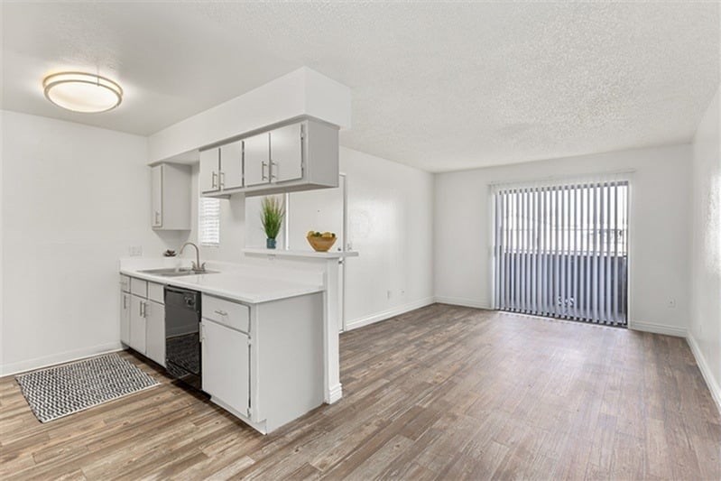 A kitchen with white cabinets and a white countertop with a sink and a window with blinds.