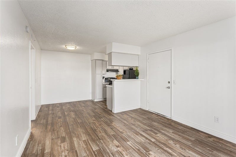 A room with a white ceiling and wooden flooring with a white cabinet and a plant on top.