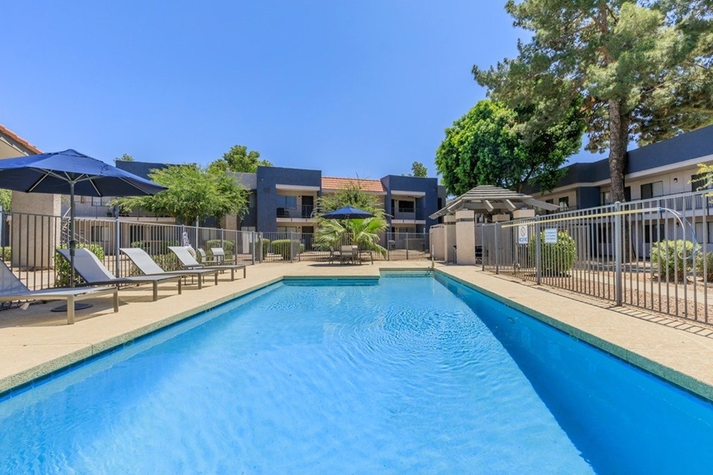 A large blue swimming pool surrounded by lounge chairs and umbrellas.