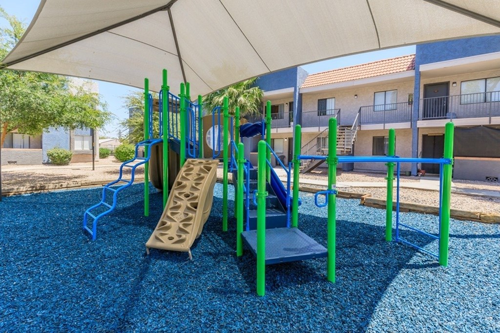 A playground with a blue rubber surface and a green and blue play structure.