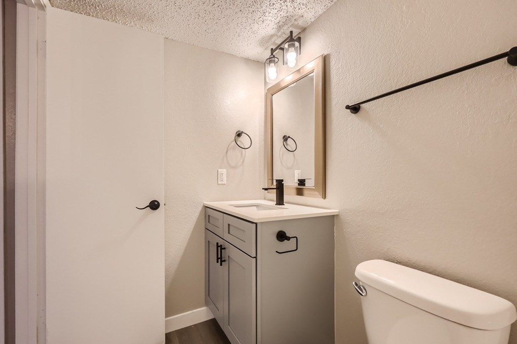 A white bathroom with a sink, mirror, and toilet.