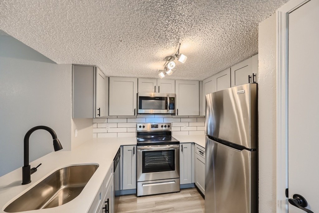 A kitchen with a stainless steel refrigerator, oven, and sink.