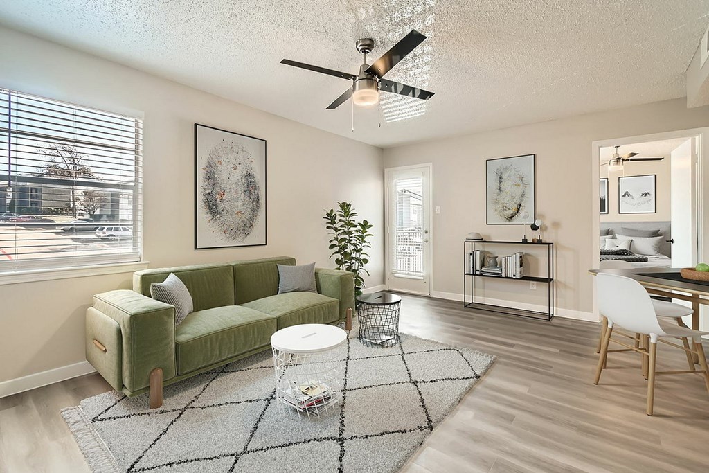 A living room with a green couch, a white chair, and a ceiling fan.