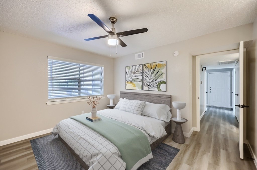 A bedroom with a bed, a ceiling fan, and a painting on the wall.