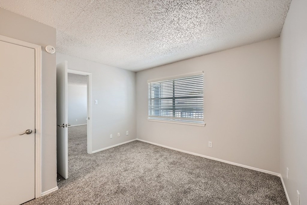 A room with a carpeted floor and a window with blinds.