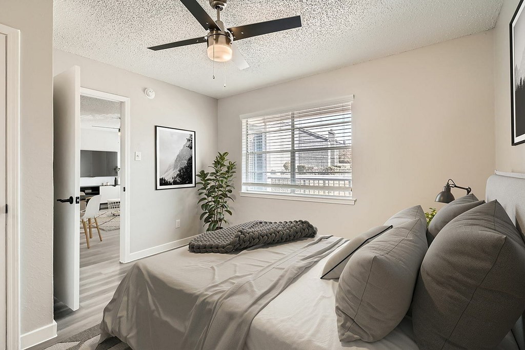 A bedroom with a bed, pillows, a ceiling fan, and a window with blinds.