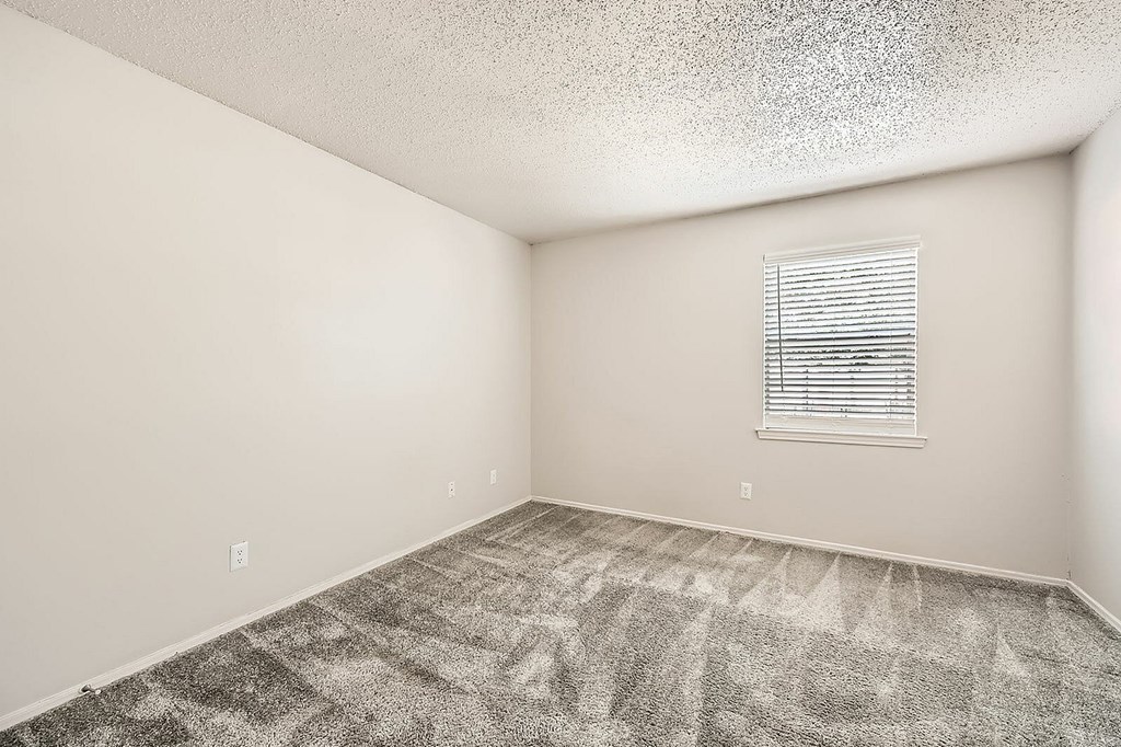 A room with a carpeted floor and a window with blinds.