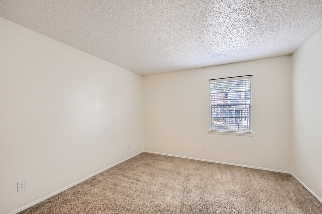 A room with a carpeted floor and a window with blinds.