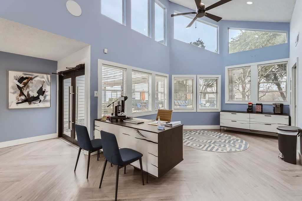 A room with a desk, chairs, and a ceiling fan.