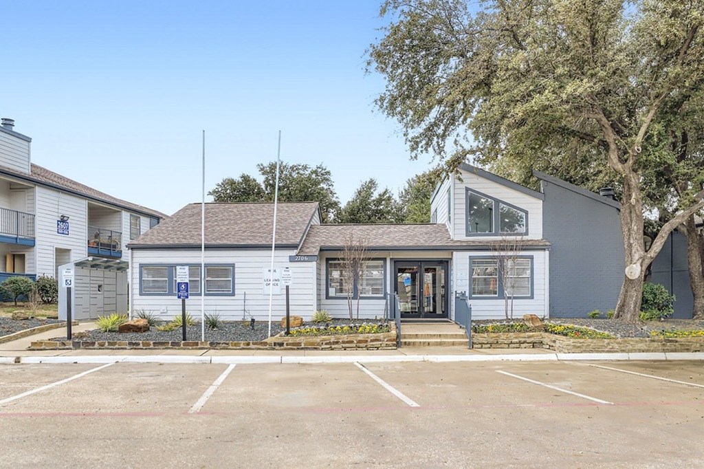 A small building with a grey roof and a parking lot in front.