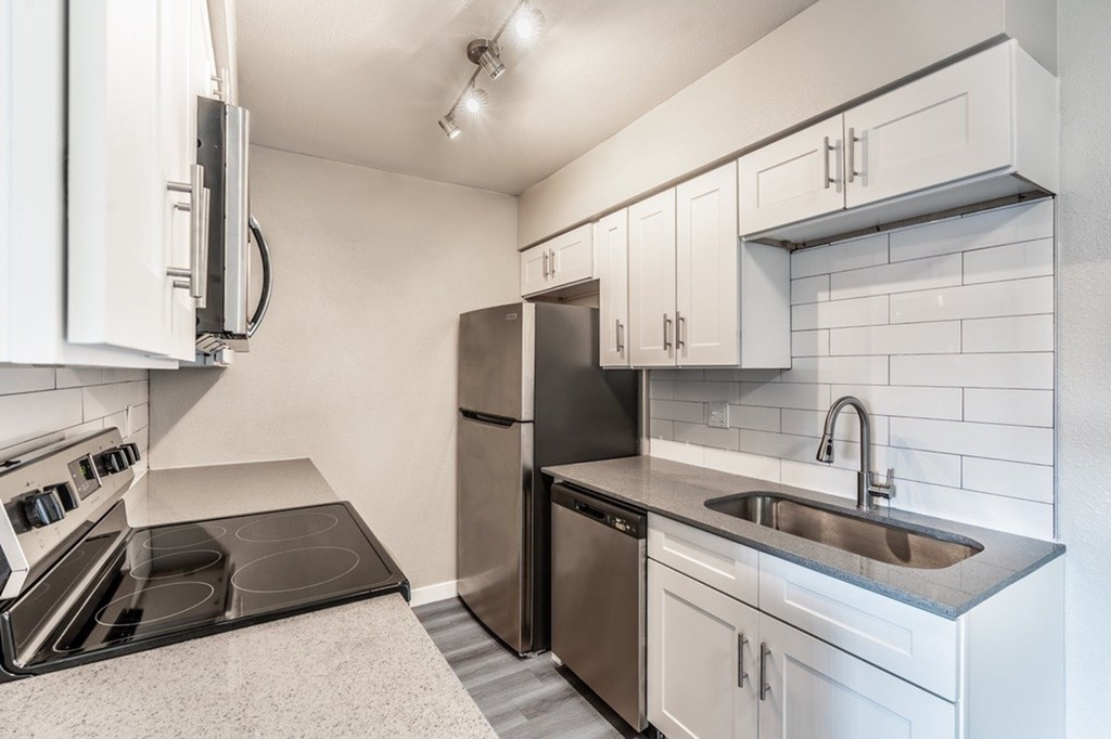 A kitchen with a black refrigerator, stove, and white cabinets.