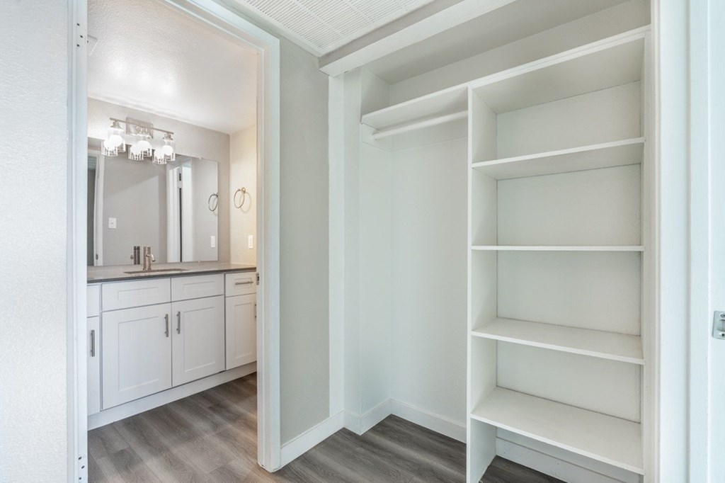 A white closet with shelves and a mirror in the background.