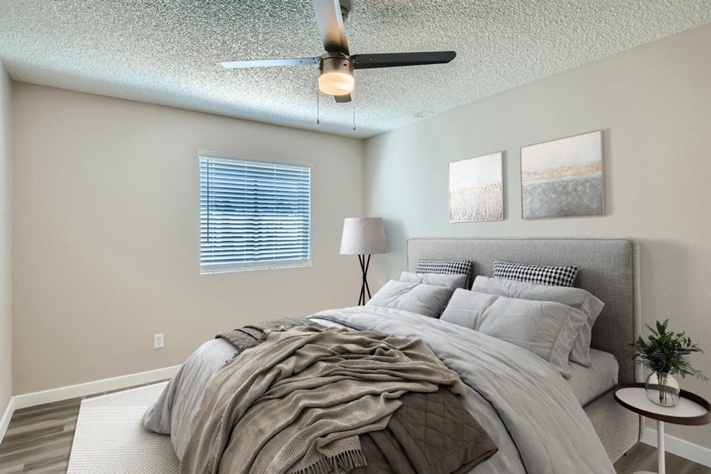 A bedroom with a bed, a ceiling fan, and a small table with a plant on it.