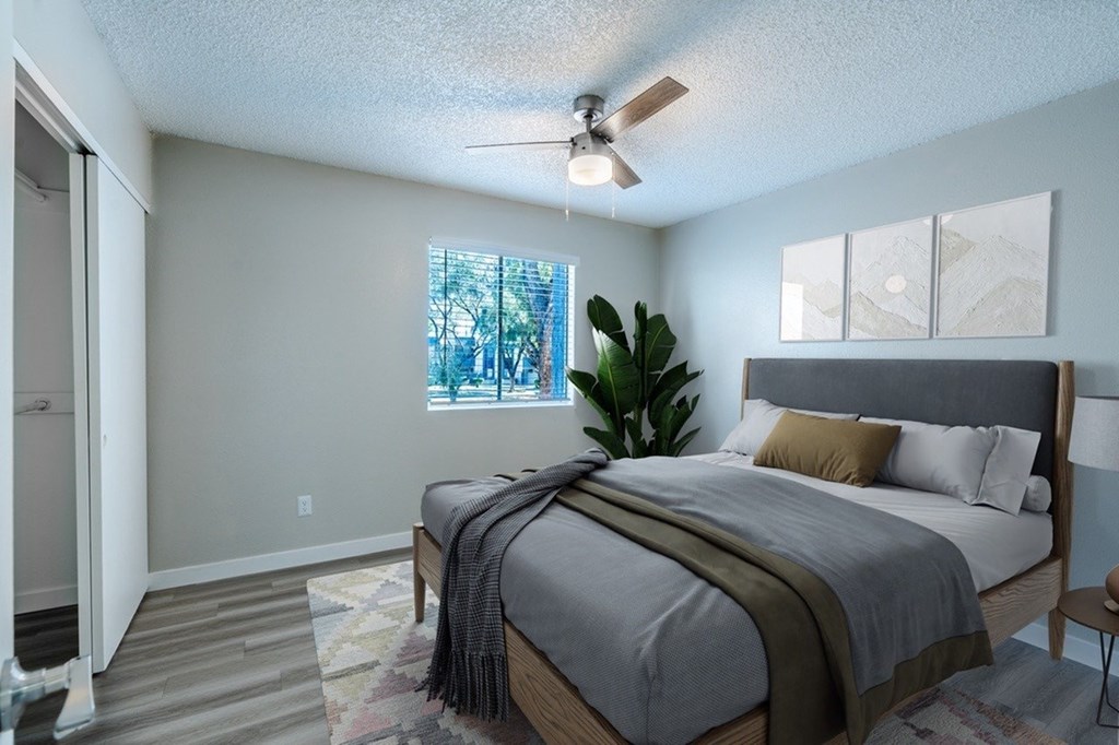A bedroom with a bed, a ceiling fan, and a window with a view of trees.