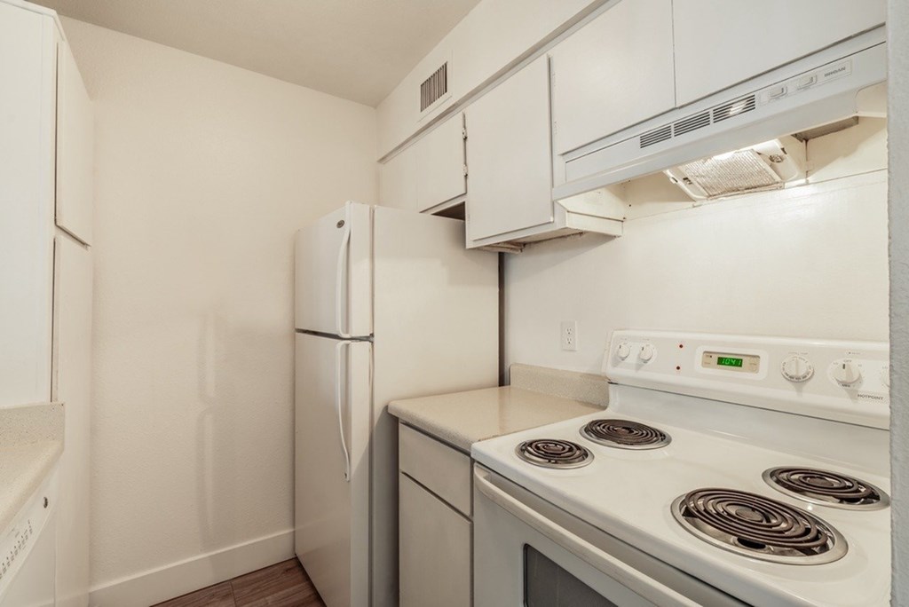 A white kitchen with a stove top oven and a refrigerator.