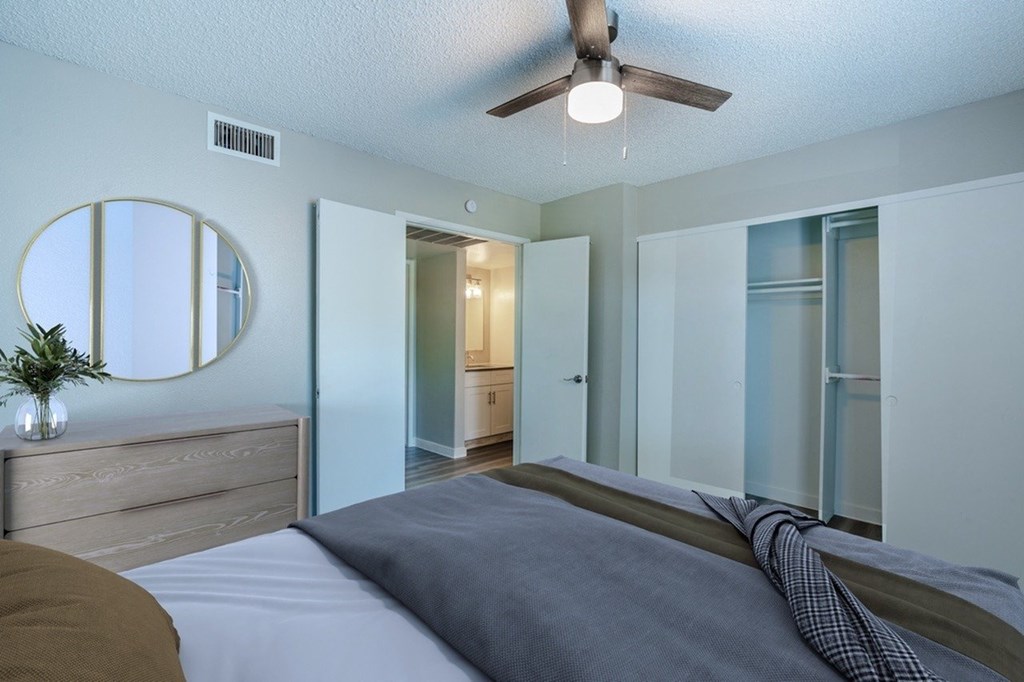 A bedroom with a bed, dresser, mirror, and ceiling fan.