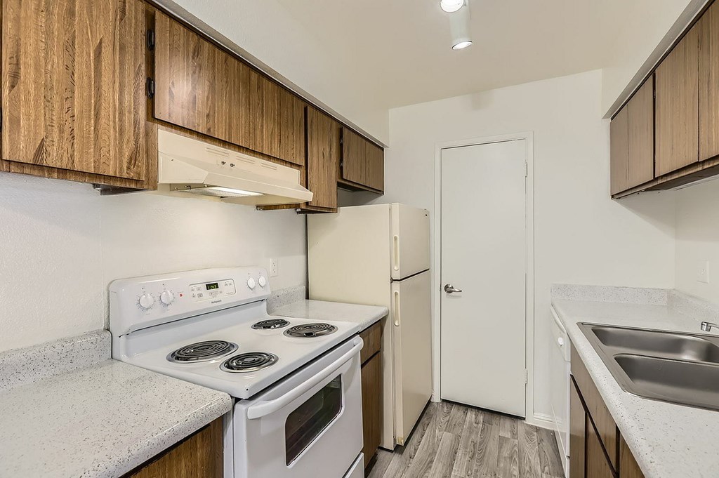 A kitchen with a white stove top oven, white refrigerator, and white sink.
