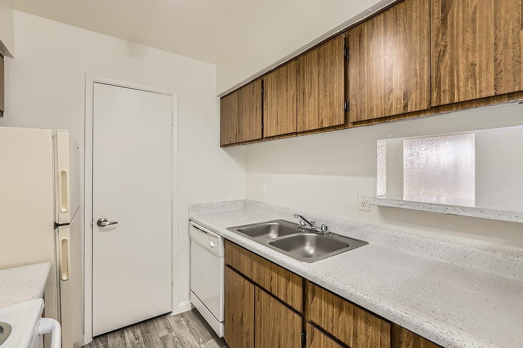 A kitchen with a white fridge, wooden cabinets, and a white sink.