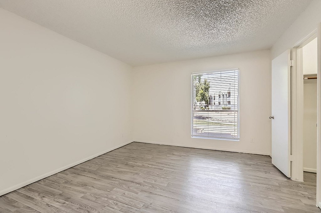 A room with a window covered by blinds and a wooden floor.