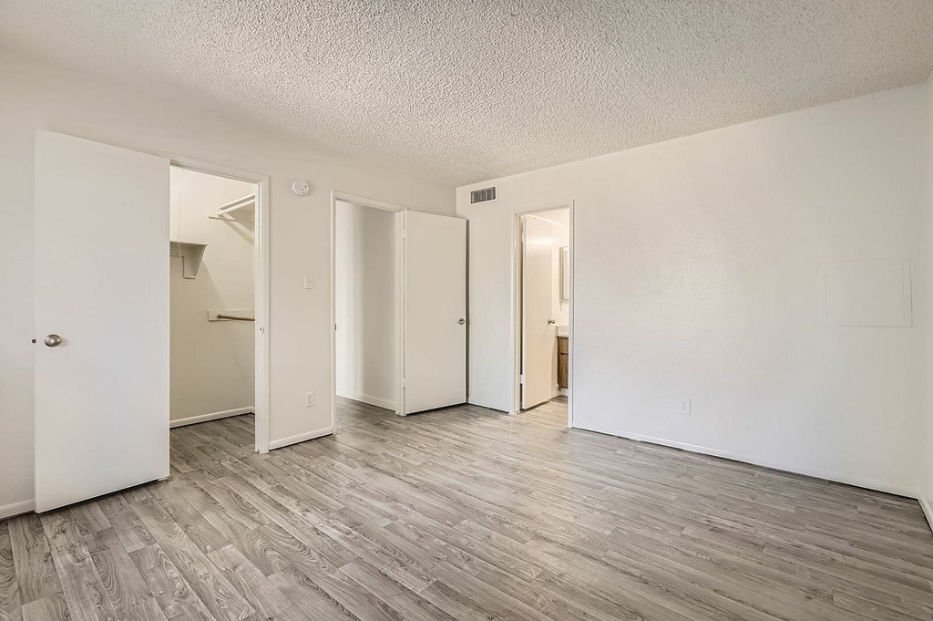 A room with white walls and wood flooring with four doors.