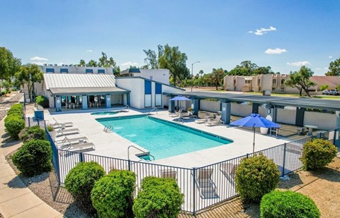 A swimming pool surrounded by a fence and bushes with a building in the background.