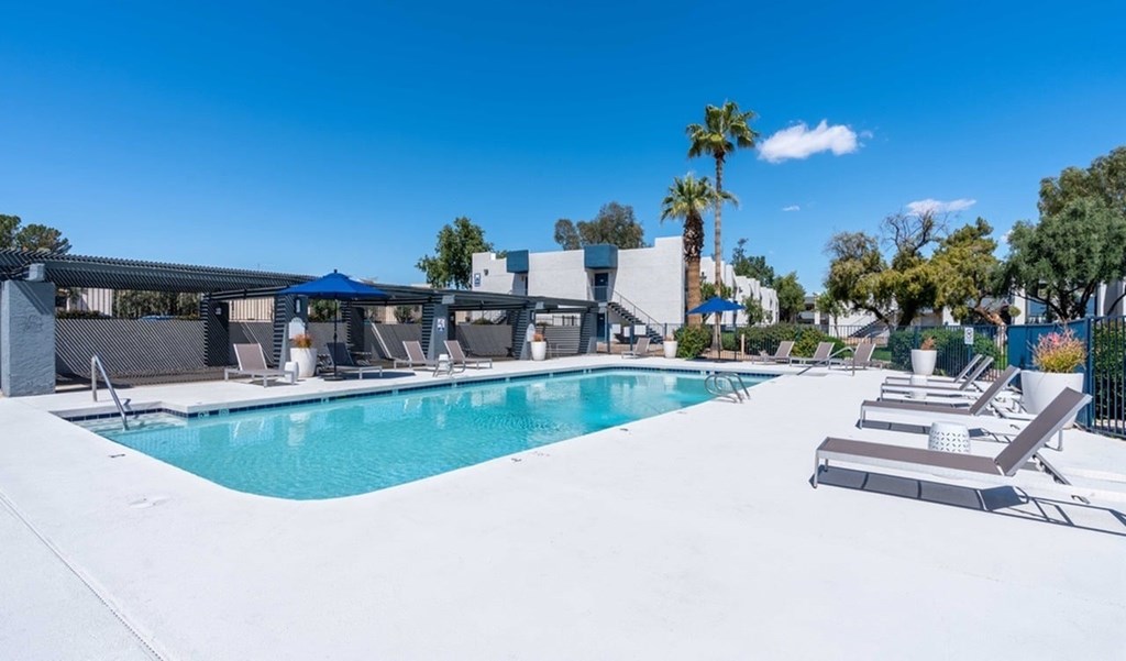 A swimming pool surrounded by lounge chairs and palm trees.