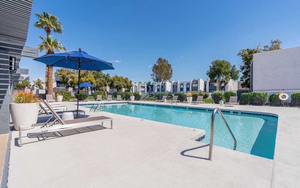 A pool with a blue umbrella and lounge chairs.