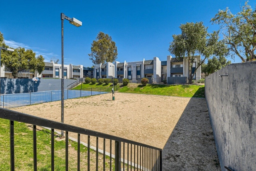 A sandy area with a fence and a building in the background.