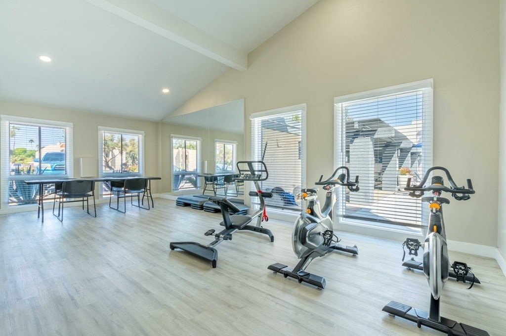 A spacious room with a row of stationary bikes and a table with chairs.