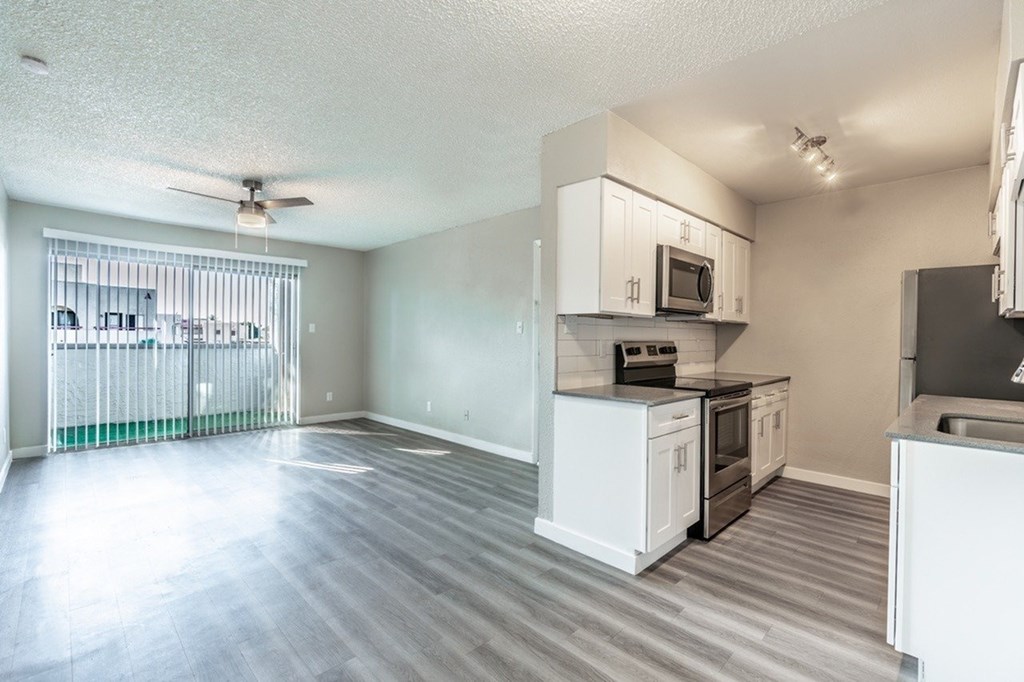 A spacious kitchen and living room with white appliances and wood flooring.