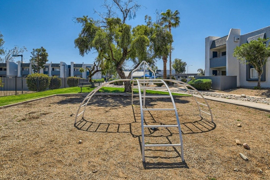 A playground with a ladder and a tree in the middle of a gravel area.