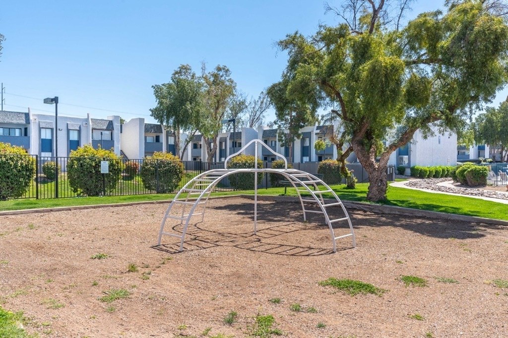 A playground with a swing set in the foreground and apartment buildings in the background.