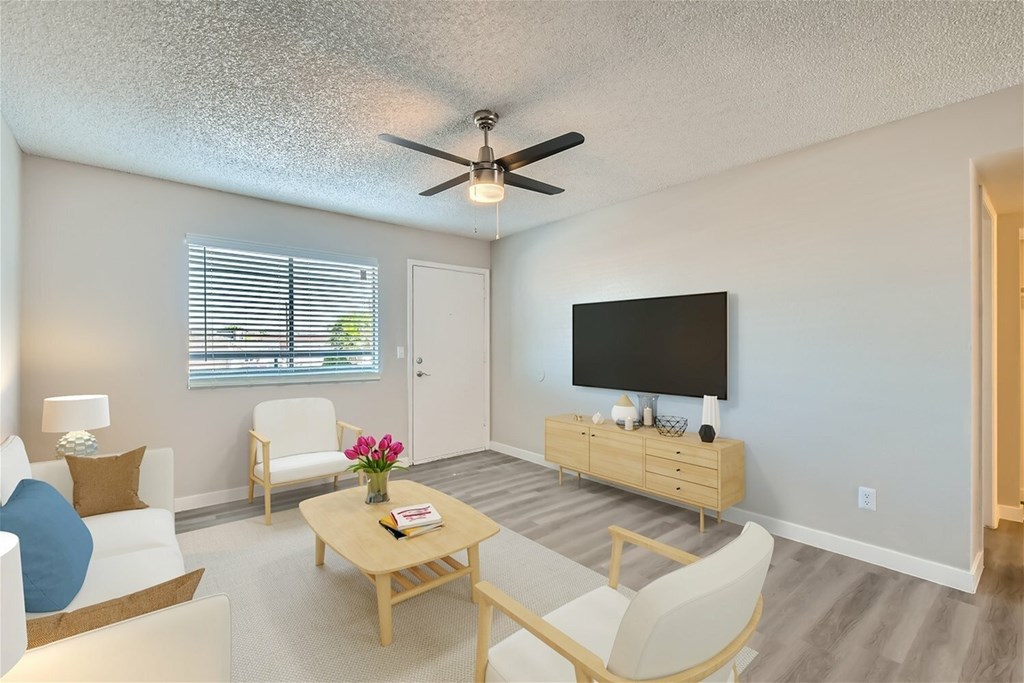 A living room with a white couch, a wooden coffee table, and a flat screen TV mounted on the wall.