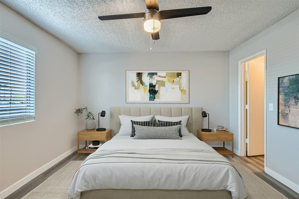 A bedroom with a large bed, a ceiling fan, and a painting on the wall.