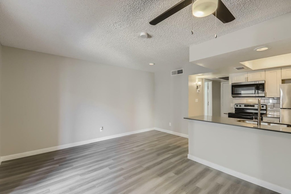 A spacious room with a ceiling fan and a kitchenette in the corner.