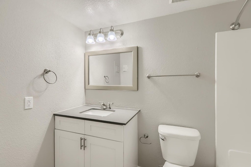 A white bathroom with a sink, mirror, toilet, and a shower.