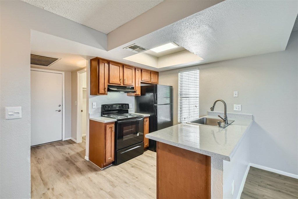 A kitchen with a black refrigerator and wooden cabinets.