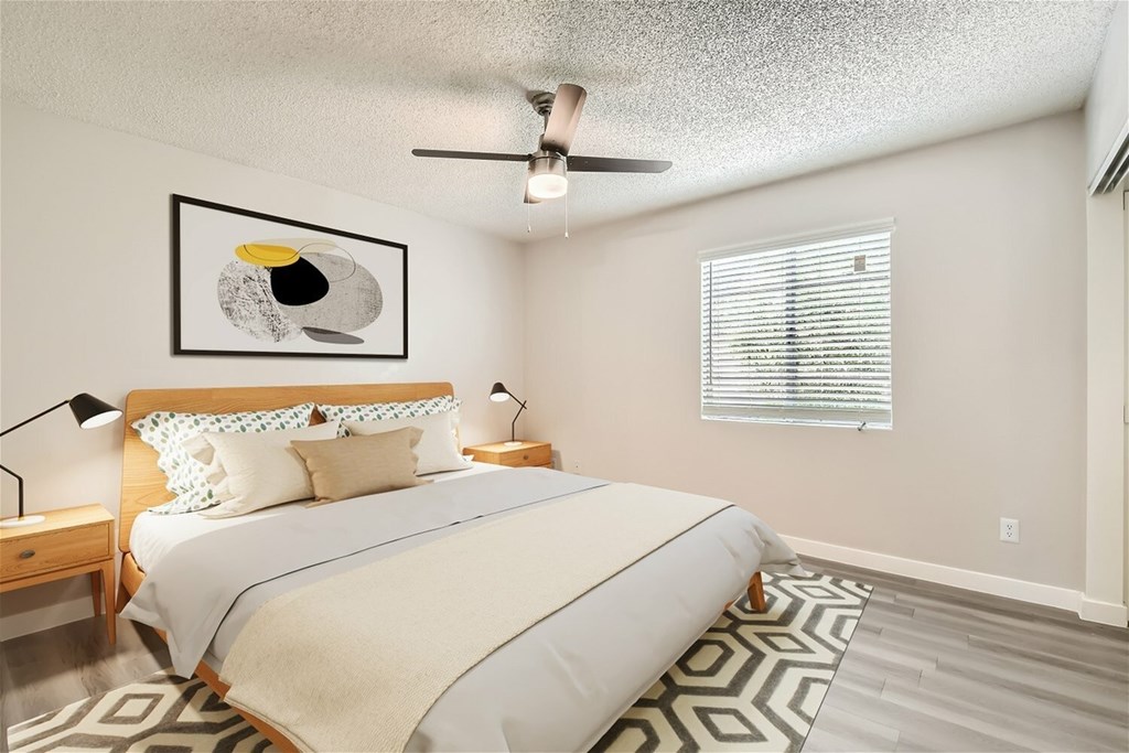 A bedroom with a bed, a ceiling fan, and a painting on the wall.