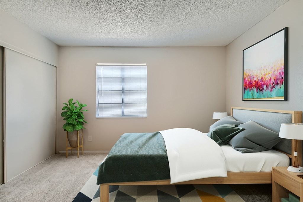 A bedroom with a bed, a lamp, a potted plant, and a painting on the wall.