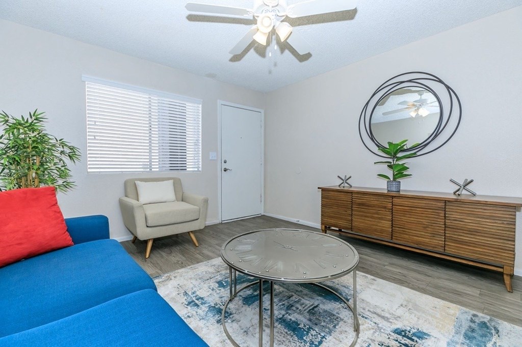 A blue sofa sits in a living room with a round table and a mirror on the wall.