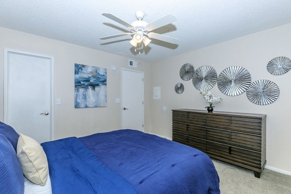 A bedroom with a blue bedspread and a ceiling fan.