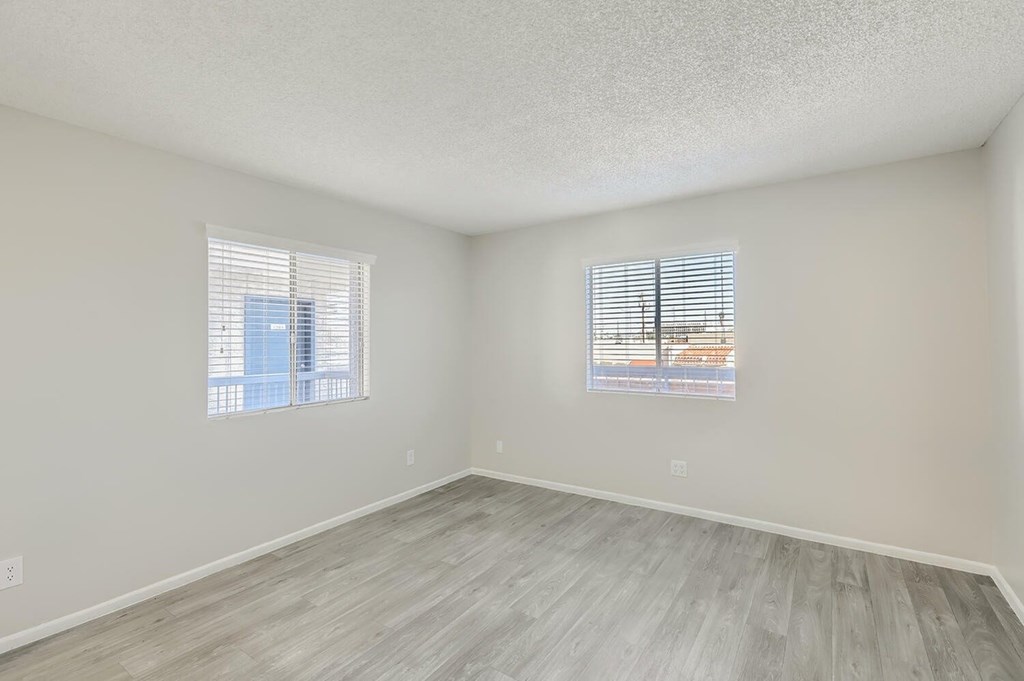A room with light grey flooring and two windows with blinds.