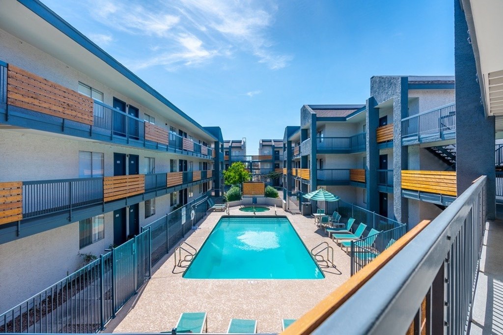 A swimming pool is surrounded by chairs and umbrellas in a courtyard.