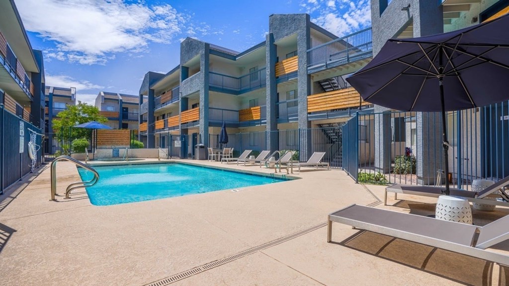 A swimming pool surrounded by lounge chairs and umbrellas in a sunny outdoor setting.