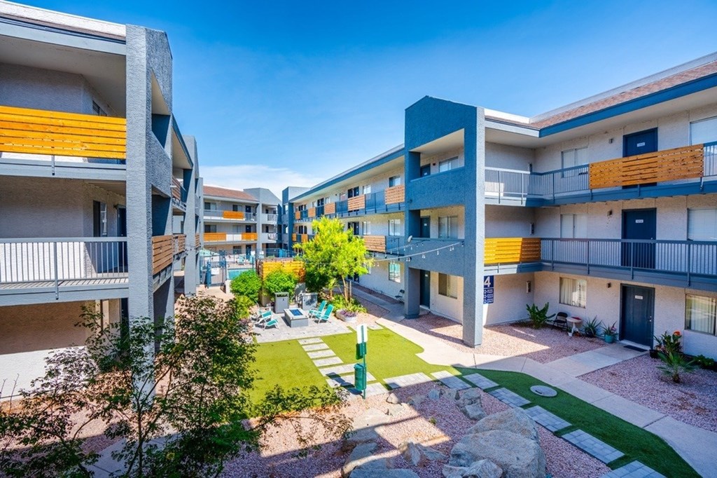 A sunny day at a modern apartment complex with a green lawn and trees.
