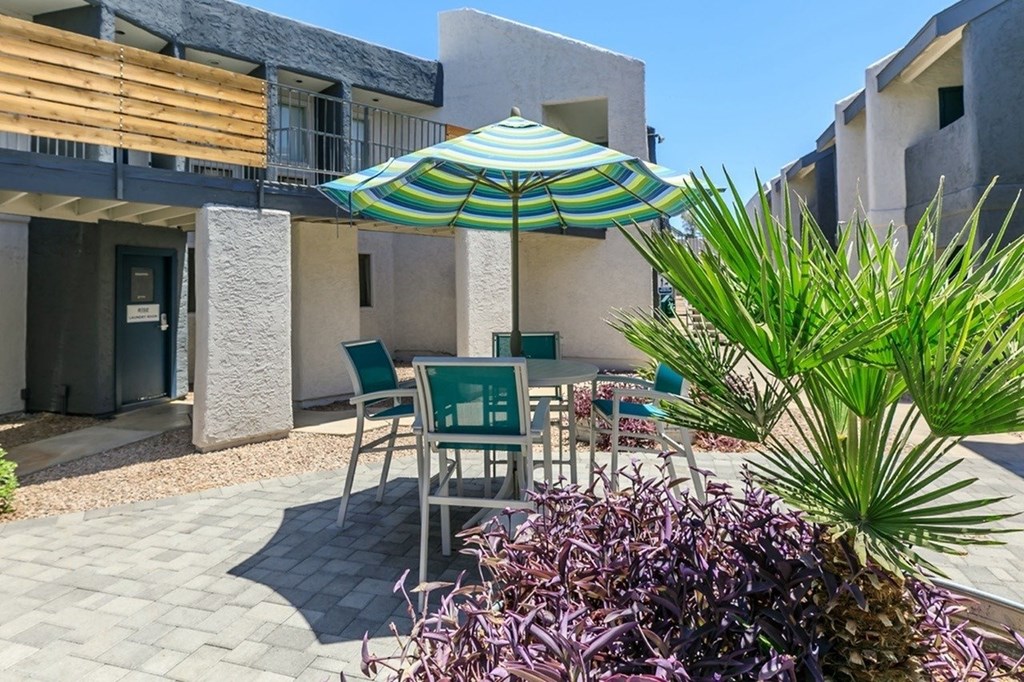 A patio with a green umbrella and a pineapple plant.